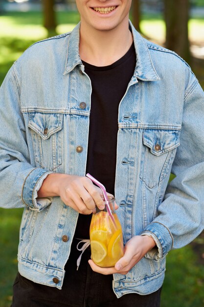 Healthy youth lifestyle. Happy hipster guy with detox with sweet citrus detox tea or orange juice in summer, on green nature background