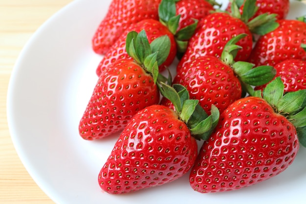 Heap of bright red color fresh ripe strawberries on a white plate