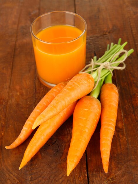 Heap of carrots glass of juice on wooden background