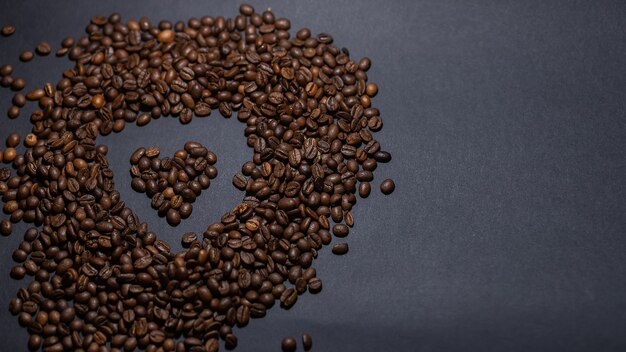 Heap of coffee beans on black background. Coffee beans pile isolated on black background. Culinary coffee background. heart shaped coffee beans top view