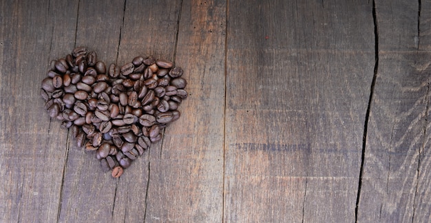 Mucchio di chicchi di caffè che formano un cuore su una tavola rustica con copia sapce a destra