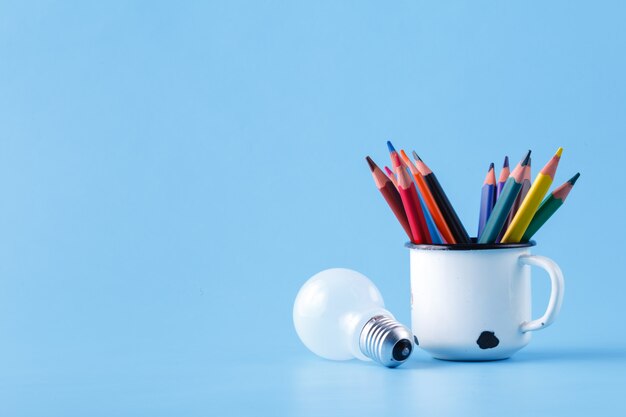 Heap of colour pencils and light bulb on blue surface