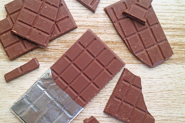 Heap of cracked chocolate bars scattered on wooden table