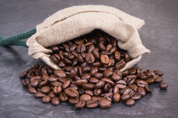 Heap of dark roasted coffee grains in jute bag