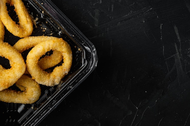 Mucchio di calamari fritti o anelli di cipolla pacchetto su pietra nera scura sfondo tavolo vista dall'alto piatto con spazio di copia per il testo