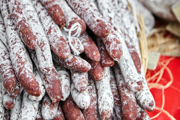 Heap of dry-cured sausages with white mold on the counter of the farmers market