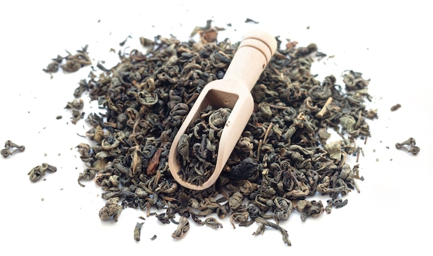 Heap of dry green tea with bamboo scoop isolated