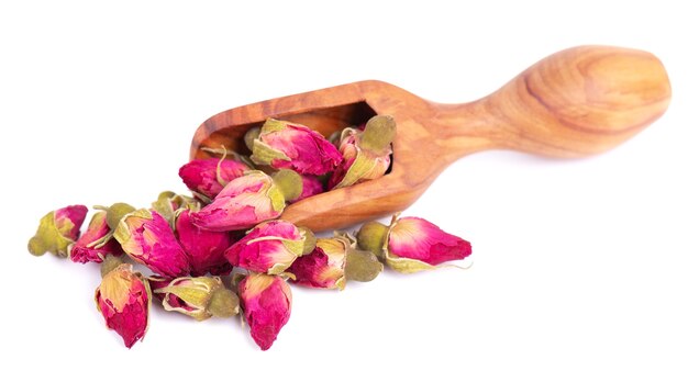 Heap of dry tea roses buds in wooden scoop, isolated on white background. Rose flower tea. Clipping path.