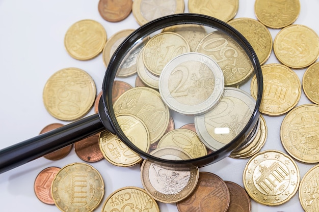 Heap of euro cents and a magnifier on a white surface.