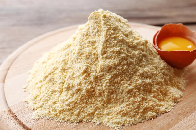 Heap of flour on cutting board with egg on wooden table