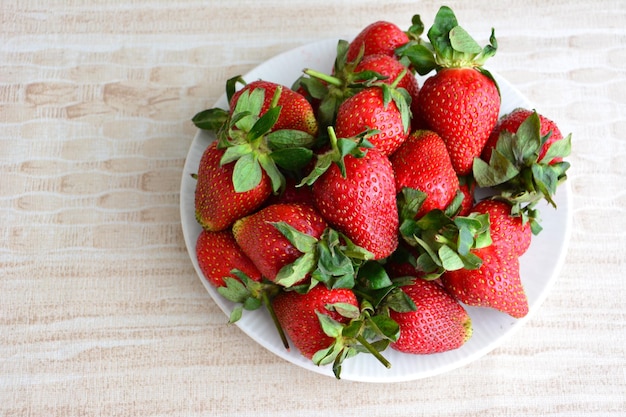 heap of fresh garden strawberries isolated on white plate on beige background, close-up