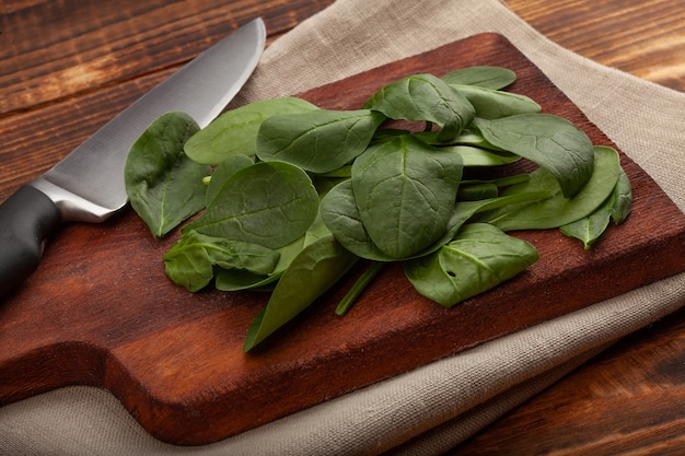 Heap of fresh green spinach and kitchen knife on the wooden board