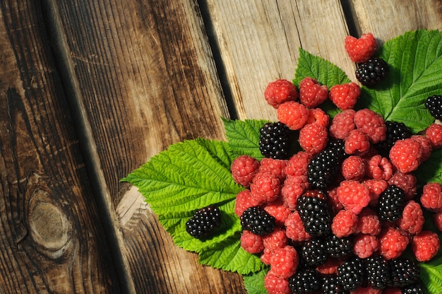 Heap of fresh raspberries and blackberries with leaves on a wooden brown table, copy space