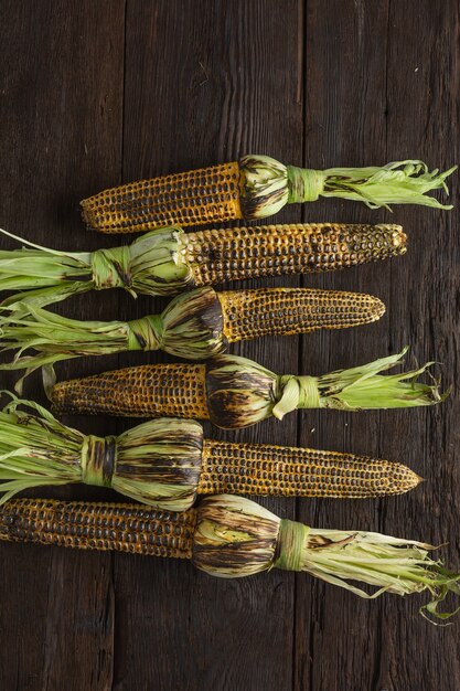 Heap of grilled corn on a wooden table, top view