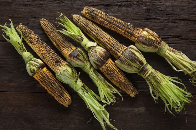 Heap of grilled corn on a wooden table, top view