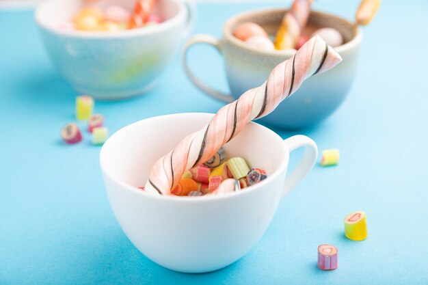 Heap of multicolored caramel candies in cups on blue background side view selective focus