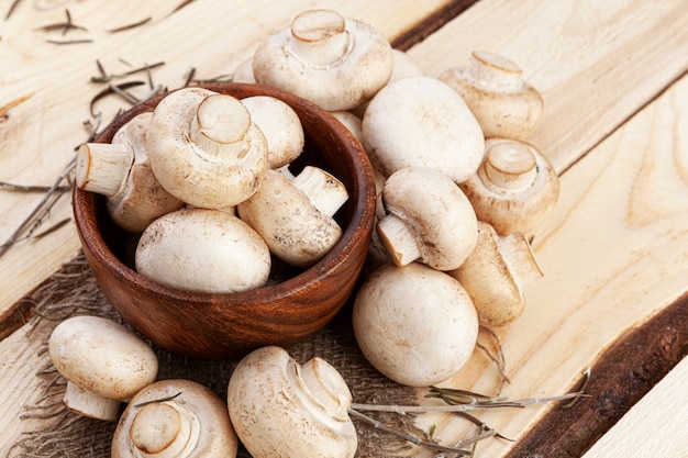 Photo heap of mushrooms, champignons in bowl on wooden table, top view