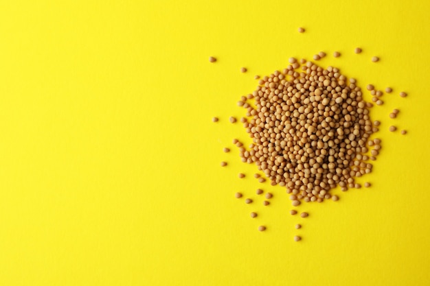 Heap of mustard seeds on yellow background, space for text