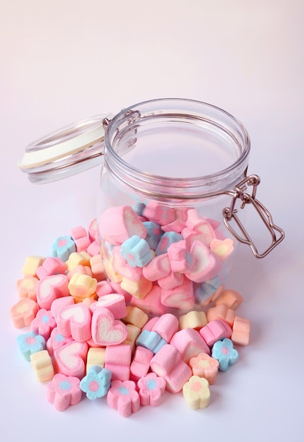 Фото Куча пастельных цветовых конфет на бледно-фиолетовом столе с некоторыми в открытой стеклянной банки