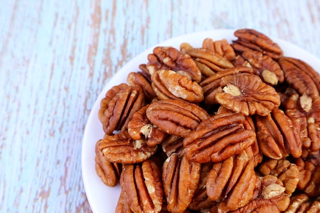 Heap of Pecan Nuts on a Plate Isolated on Pale Blue Wooden Background
