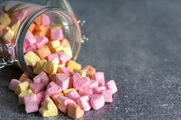 Heap of pink and yellow colorful heart shaped marshmallow candies scattered from a glass jar on gray background with copy space