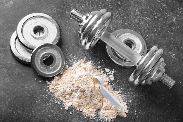 Heap of protein powder with scoop dumbbell and disks on table