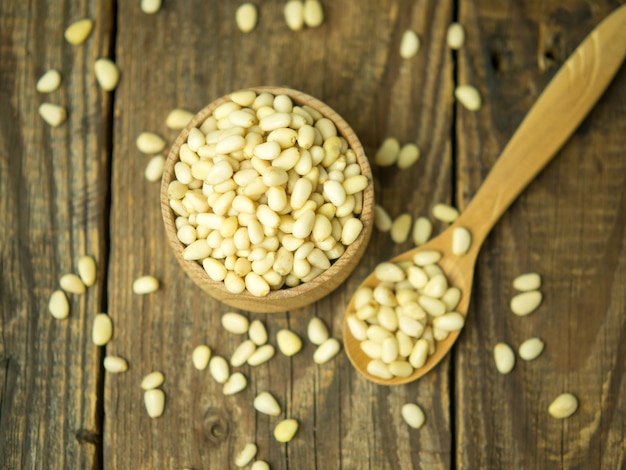 Heap of raw pine nuts in a wooden bowl and spoon Peeled pine nuts on an old wooden table