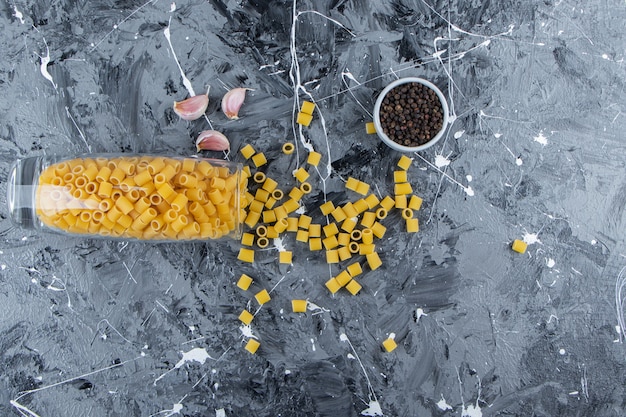 Heap of raw pipette rigate pasta in a glass jar with pepper corns and garlic. 