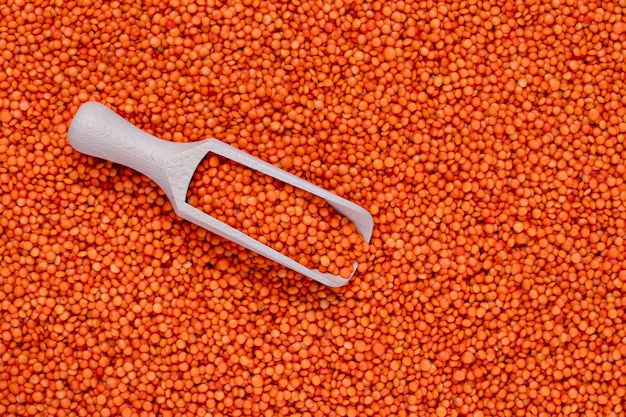 A heap of scattered red lentils and wooden scoop, top view. Seeds of legume. Kernels background, grain texture, view from above.