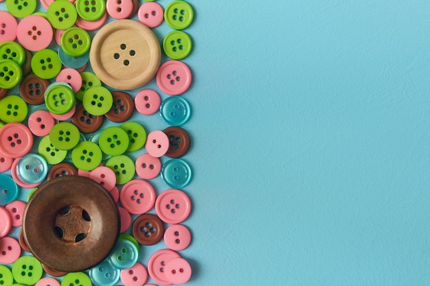 Heap sewing buttons on cyan surface. Flat lay with copy space