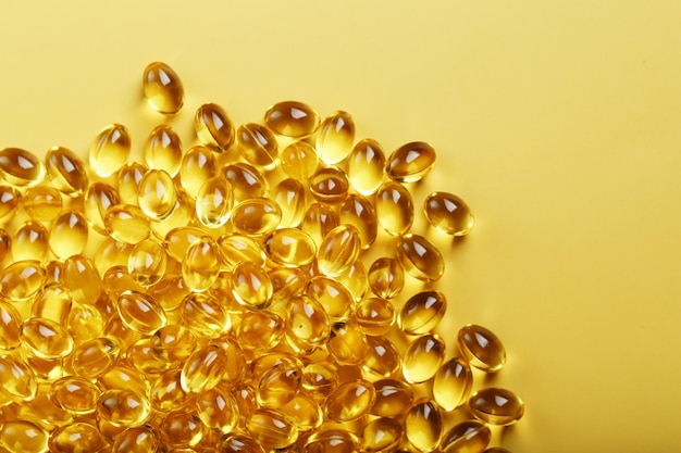 Heap of transparent fish oil capsules on yellow background with free space