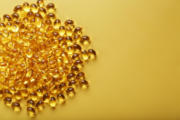 Heap of transparent fish oil capsules on yellow background with free space