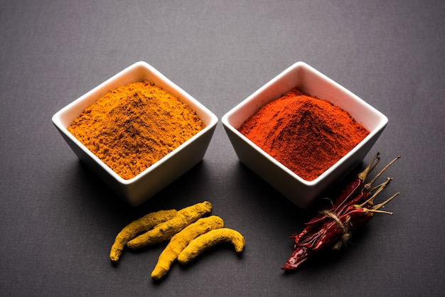 Heap of turmeric or haldi and red chilli or mirchi  powder in a ceramic bowl on a white or black surface