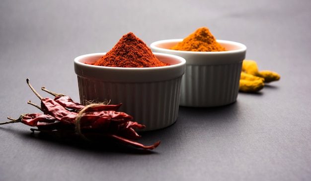 Cumulo di curcuma o haldi e peperoncino rosso o polvere di mirchi in una ciotola di ceramica su una superficie bianca o nera