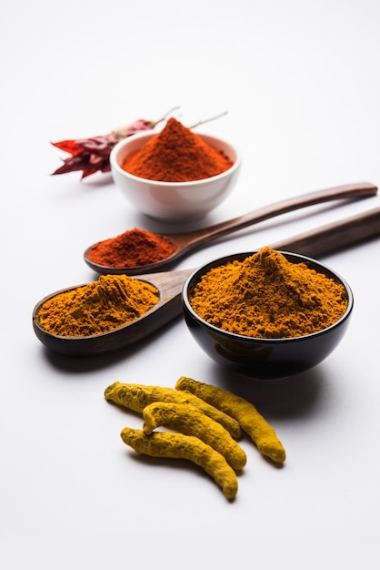 Heap of turmeric or haldi and red chilli or mirchi  powder in a ceramic bowl on a white or black surface