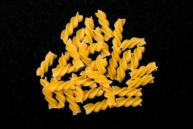 A heap of uncooked fusilli pasta scattered on black table