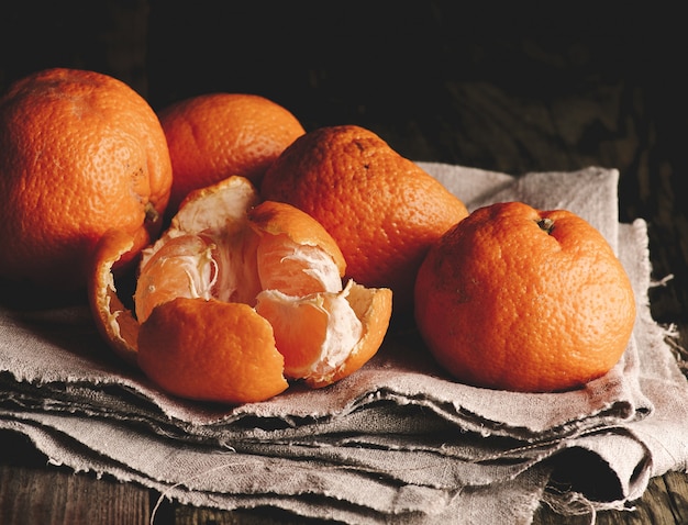 Куча неочищенного круглого спелого оранжевого мандарина на серой льняной салфетке