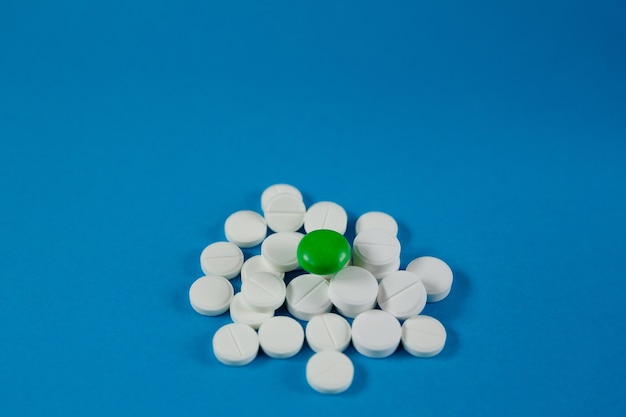 Heap of white pills and one green on a blue background