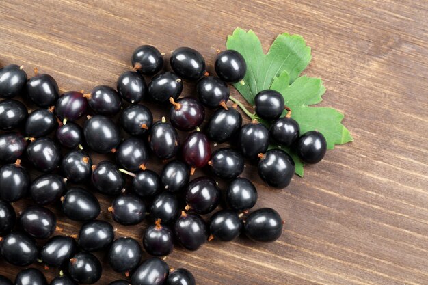 Foto mucchio di ribes nero selvatico con foglie verdi sulla tavola di legno da vicino