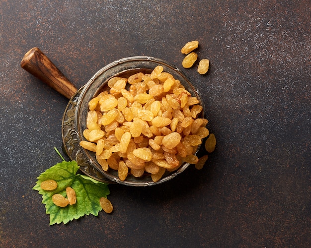 Heap of yellow raisins. Top view of dried grapes with green leaf.