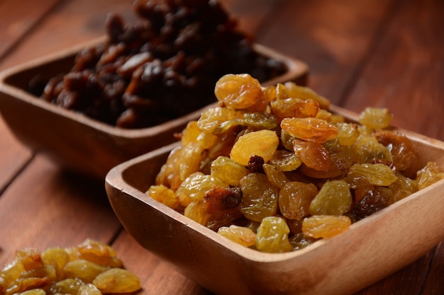 Heaps of yellow and dark Raisins, in a wooden bowls.  Dried Grapes.