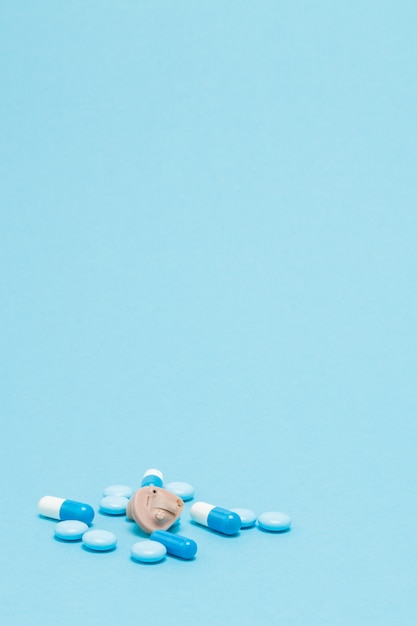 Hearing aid and blue pills on blue background