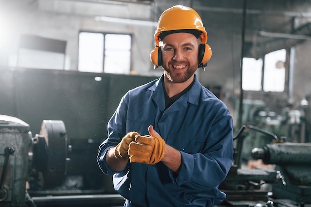 In hearing protection earphones Factory worker in blue uniform is indoors