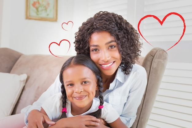 Foto cuore contro la bella madre seduta sul divano con sua figlia che sorride alla macchina fotografica