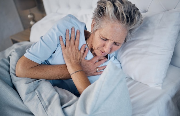 Пожилая женщина с сердечным приступом и беспокойством по поводу боли в груди или неотложной медицинской помощью в ее спальне Изжога, стресс или инсульт пожилого человека, кардиологическое дыхание и проблемы с легкими с риском для здоровья