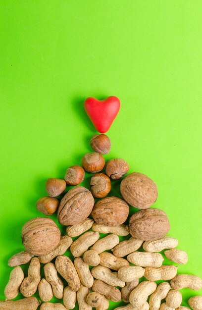 Heart and big pile of nuts on green background walnut peanut and hazelnut The concept of healthy eating