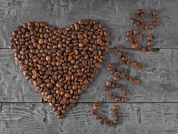 A heart of coffee beans on a black rustic table. The view from the top. Grains for the preparation of the popular drink. The view from the top.