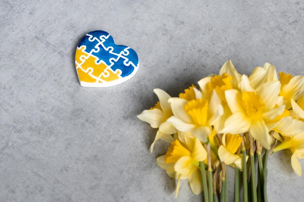 Heart in the colors of the flag of ukraine on a gray background with yellow flowers