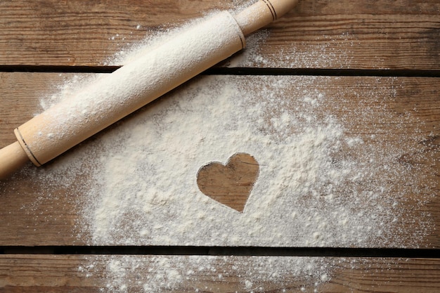 Heart drawn on flour and rolling pin on wooden background