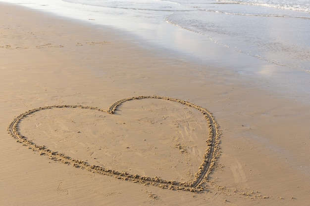 Heart drawn on a sand beach with the sea in the morning.